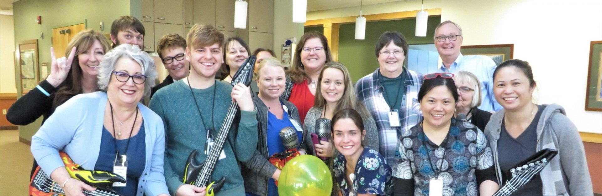 Large group of Willamette View employees posing with blow-up musical instruments and microphones.