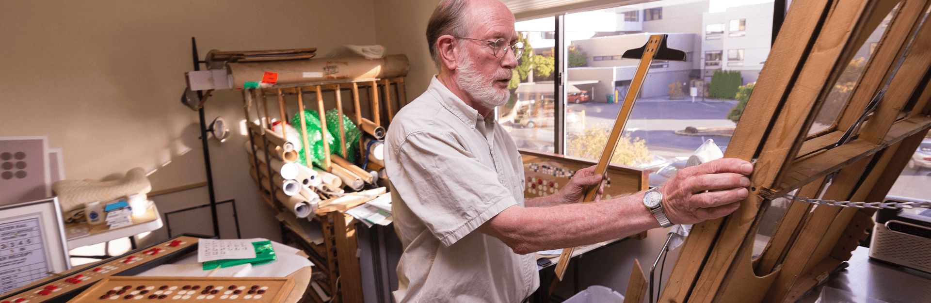 Richard is holding a T-square and looking at an easel in a studio