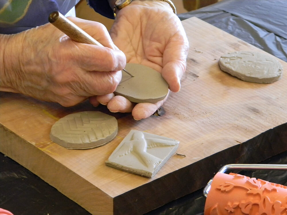 hands holding a tool that is etching into a clay form