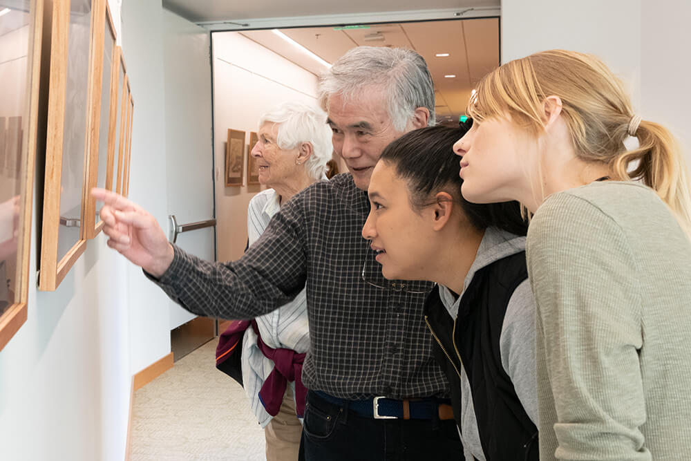 A man showing two younger women a piece of art displayed in the hallway