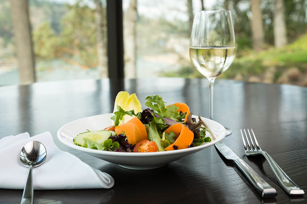 A garden salad with carrots, tomatoes and cucumber next to a glass of white wine