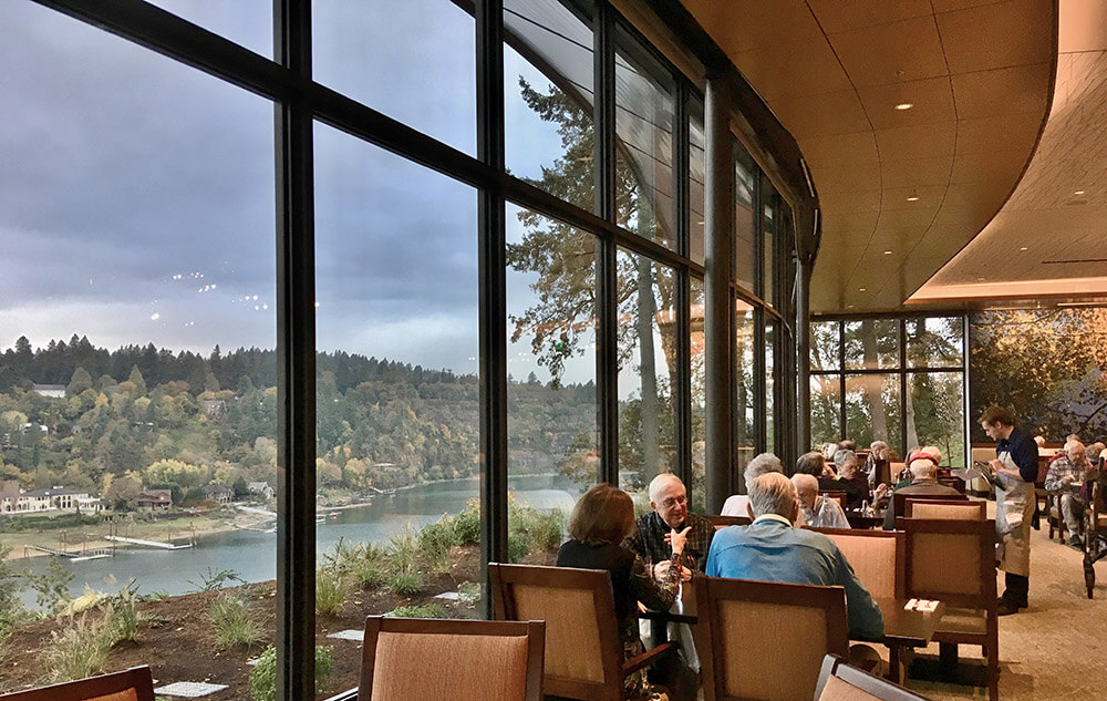 Groups of people seated at tables in the Riverview dining room with a view of the Willamette River