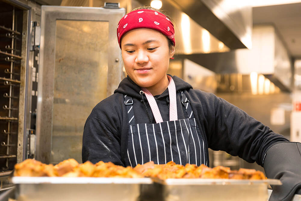 Willamette View kitchen staff member taking bread pudding out of the oven