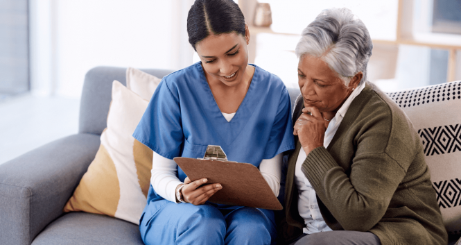 A healthcare worker reviewing information with a senior woman. Both are sitting on the couch in the senior woman's home.