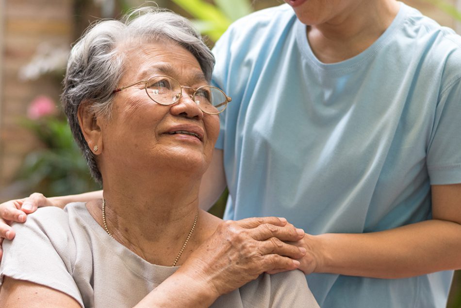 A woman in a wheelchair looking behind her towards a healthcare worker and holding her hand