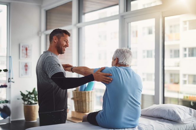 A physical therapist assessing another man's sore shoulder