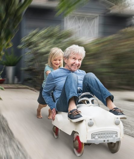 A grandchild pushing her grandmother down the driveway in a toy car