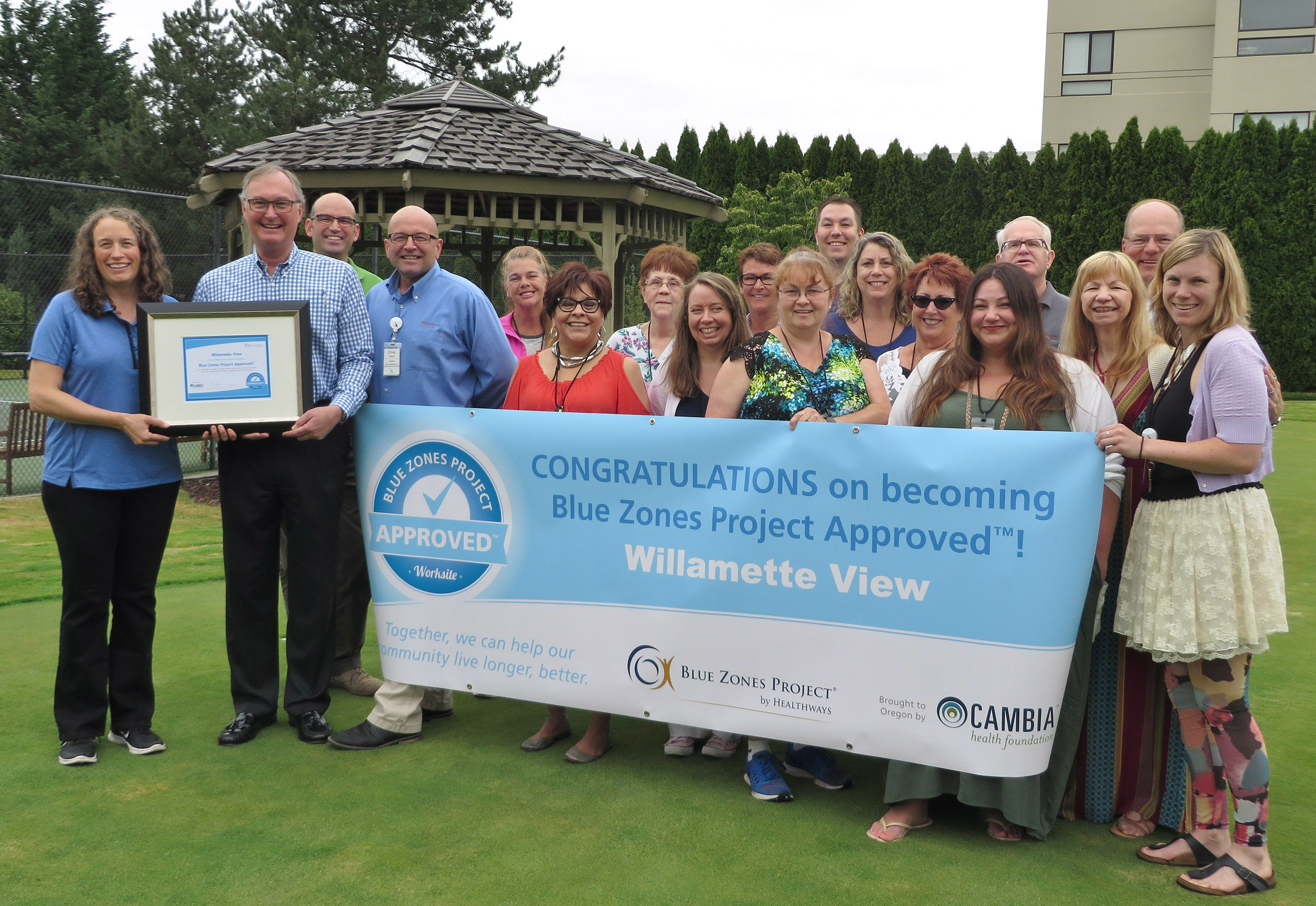 A group of Willamette View staff with a banner in front of them and a plaque signifying becoming a Blue Zone project